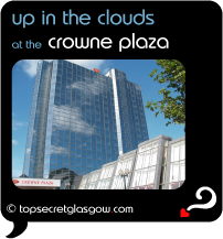 Top Secret Quote Bubble in black, with photo of crowne plaza's mirrored glass tower against a lightly cloudy  blue sky.  Caption: 'up in the clouds'