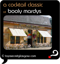 Top Secret Quote Bubble in black, with photo of exterior of Booly Mardys; blond sandstone with cream awnings and bright hanging floral baskets.  Pavement tables and chairs. Caption: 'a cocktail classic'