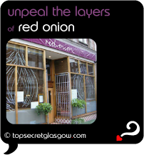 Top Secret Quote Bubble in black, with photo of exterior with topiaries and twin window vinyls of onions.  Caption: 'unpeal the layers'