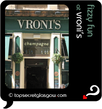 Top Secret Quote Bubble in black, with photo of entrance to Vroni's, hanging baskets either side in sunshine.  Caption: 'fizzy fun'